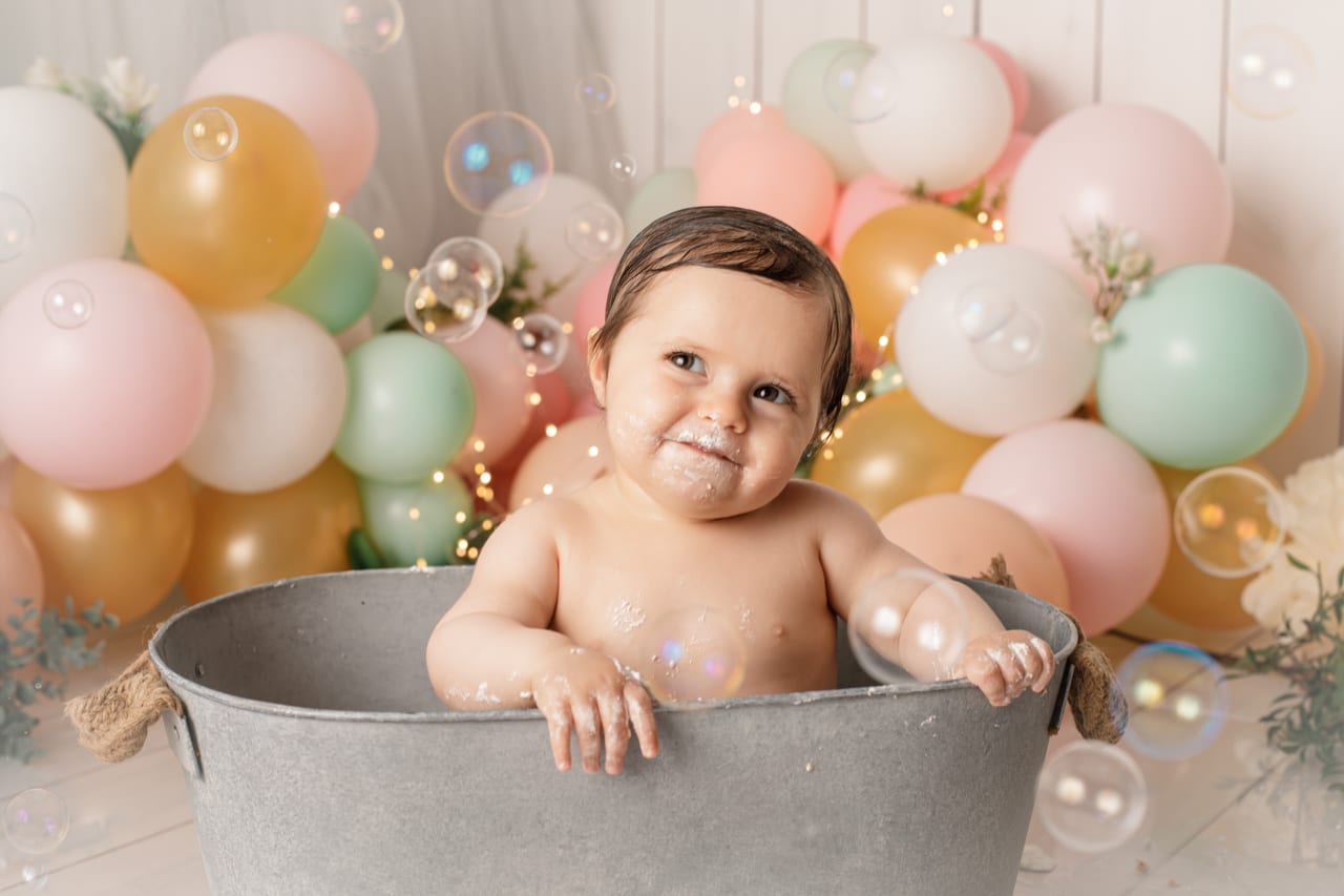 Bebé encaracolado dentro de balde de zinco com bolhas de sabão, balões pastel rosa, menta e dourado com luzes de fadas, sessão bath splash, Susana Schmitz Fotografia