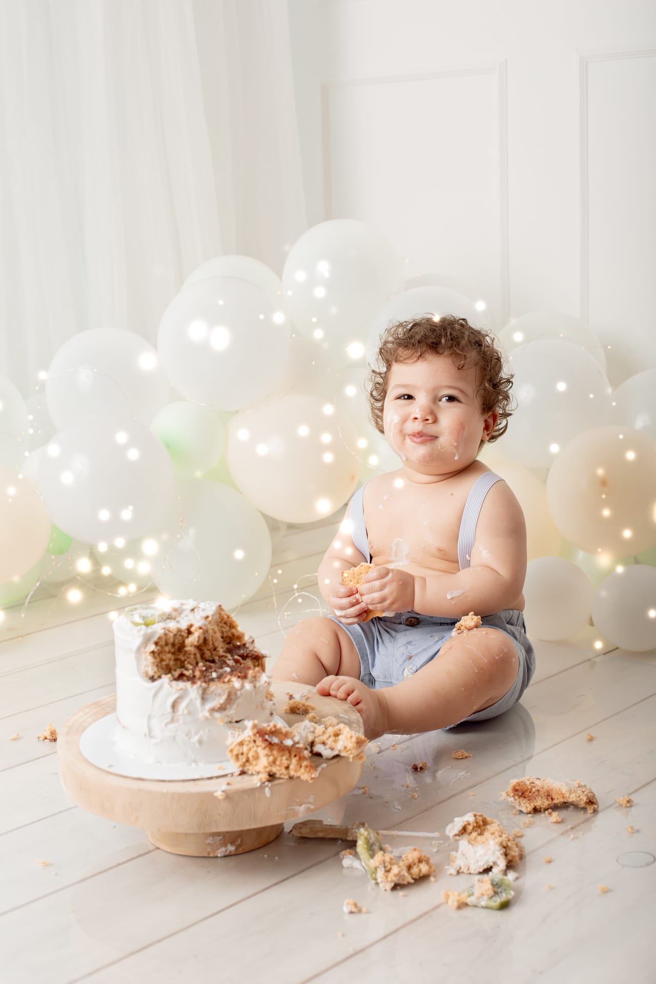Bebé sorridente com bolo branco entre arco de balões e luzes, sessão smash the cake do primeiro aniversário, Susana Schmitz Fotografia, Porto