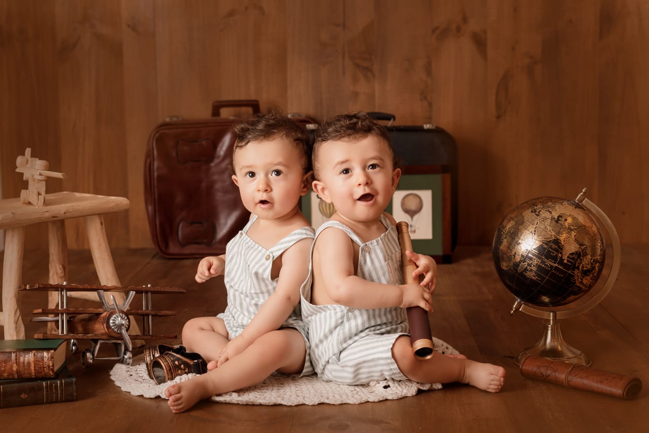 Bebés gémeos com fatos de riscas entre malas vintage, globo terrestre e avião de madeira, sessão temática de viagem em estúdio, Susana Schmitz Fotografia, Porto