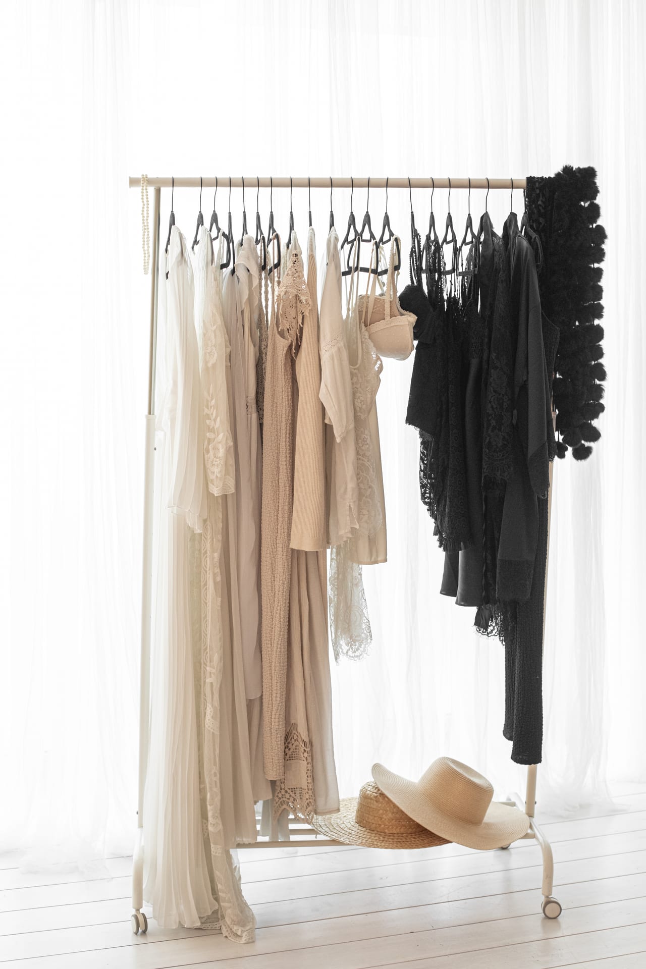 Rack de guarda-roupa de gravidez com vestidos e robes em tons cremes, beges e pretos sobre cortinado branco, estúdio Susana Schmitz, Porto