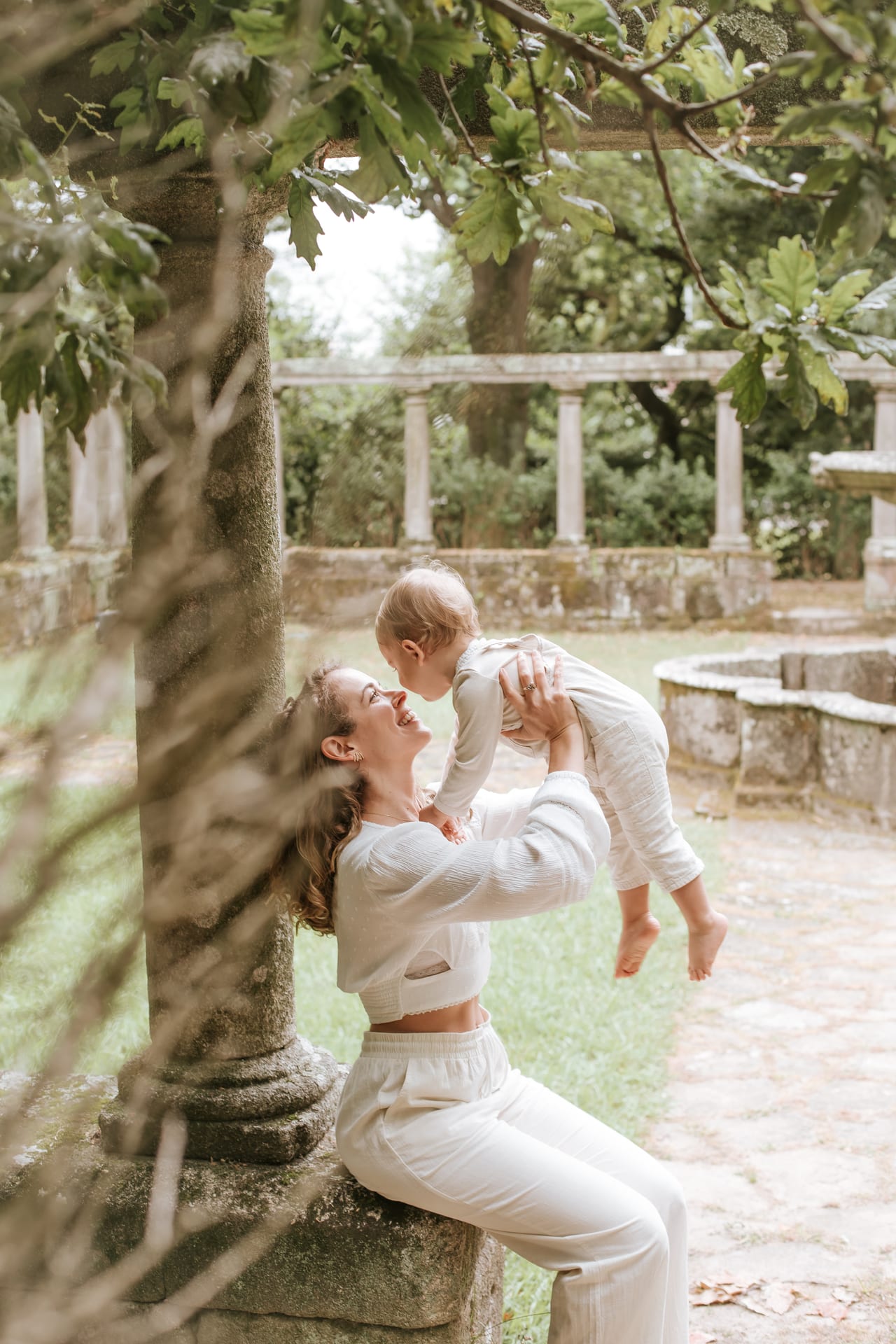 Mãe a levantar o bebé sorridente entre colunas de pedra na Quinta da Conceição, sessão de família ao ar livre, Susana Schmitz Fotografia, Porto