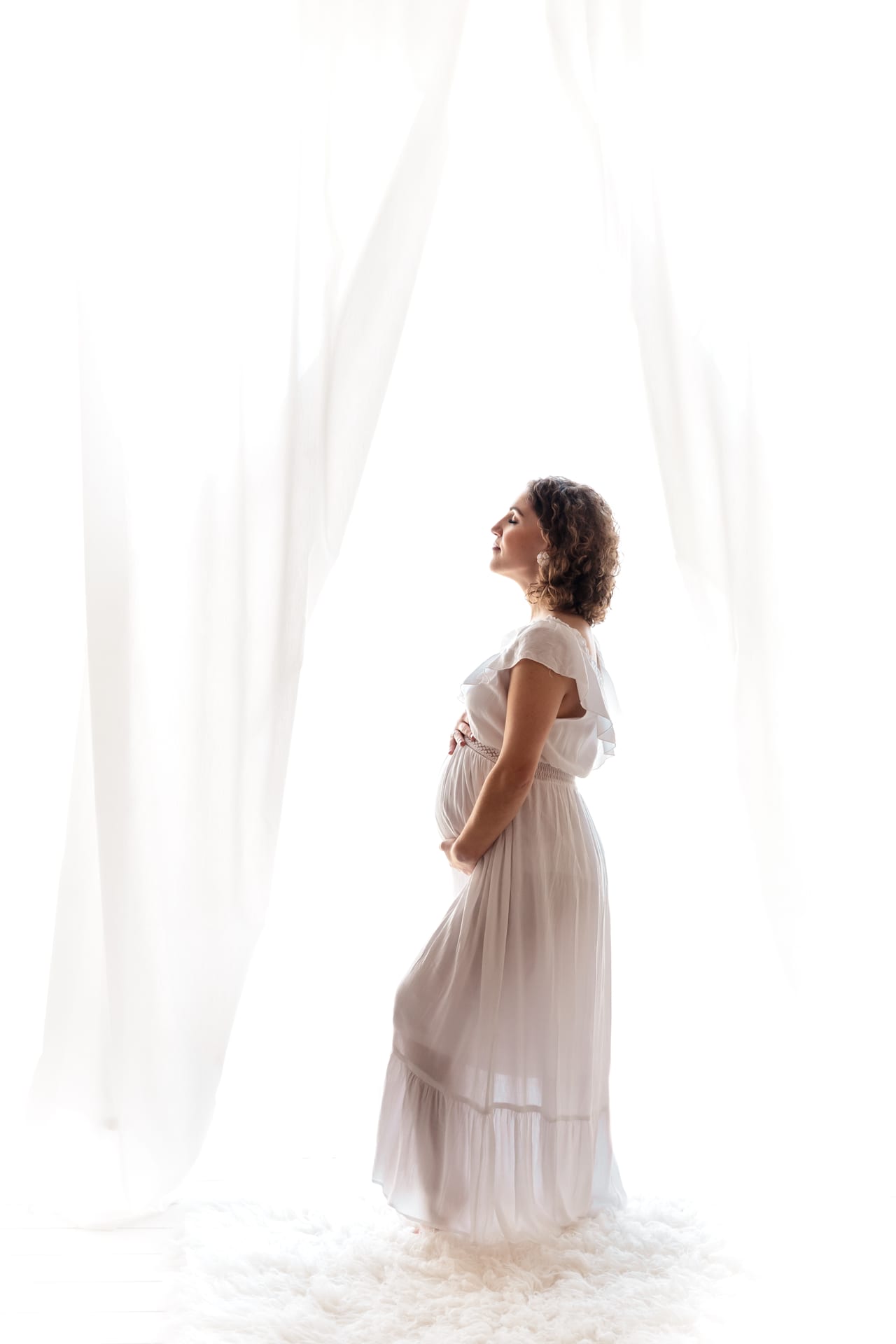 Grávida em silhueta com vestido branco esvoaçante junto a cortinas em contraluz, sessão de estúdio, Susana Schmitz Fotografia, Porto