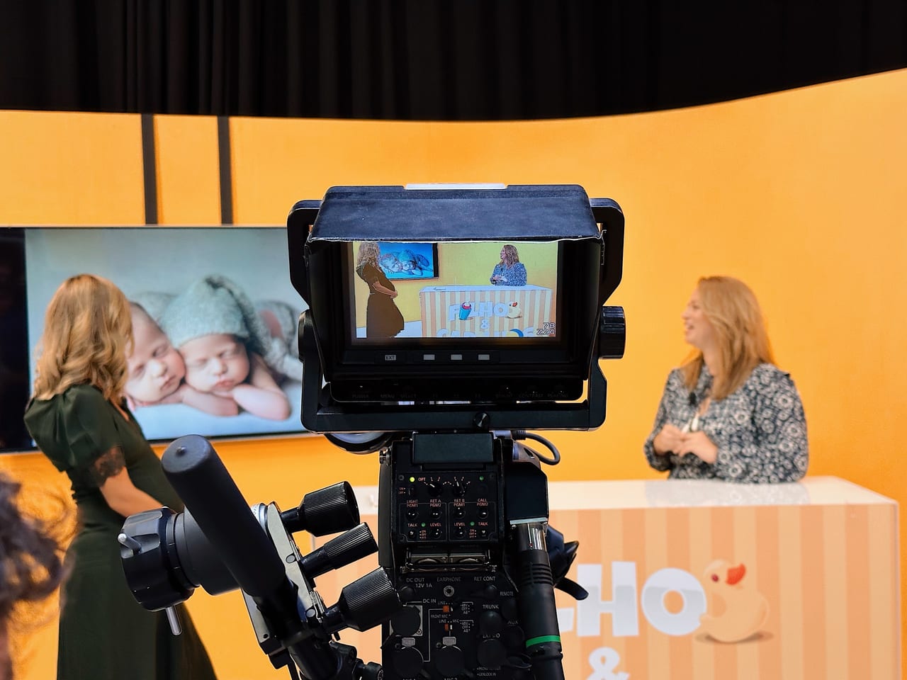 Vista através da câmara de televisão durante a gravação do programa Filhos e Cadilhos do Porto Canal com Susana Schmitz e apresentadora, fotografia de gémeos recém-nascidos no cenário, 2022