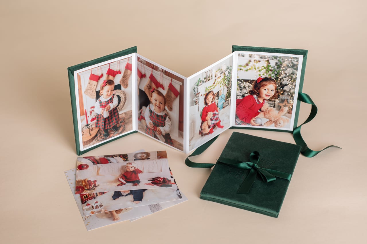 Accordion folio em veludo verde aberto em zigue-zague com impressões de sessão temática de Natal de uma criança, ao lado do mesmo folio fechado com fita de cetim verde, produto Susana Schmitz Fotografia, Porto
