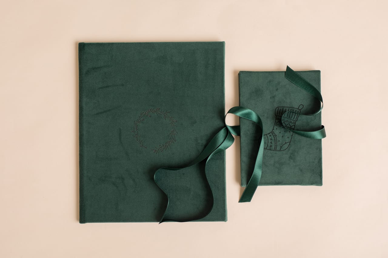 Dois folios em veludo verde fechados sobre fundo pêssego, um maior com coroa bordada e fita de cetim, outro mais pequeno com botas de Natal bordadas, produtos Susana Schmitz Fotografia, Porto