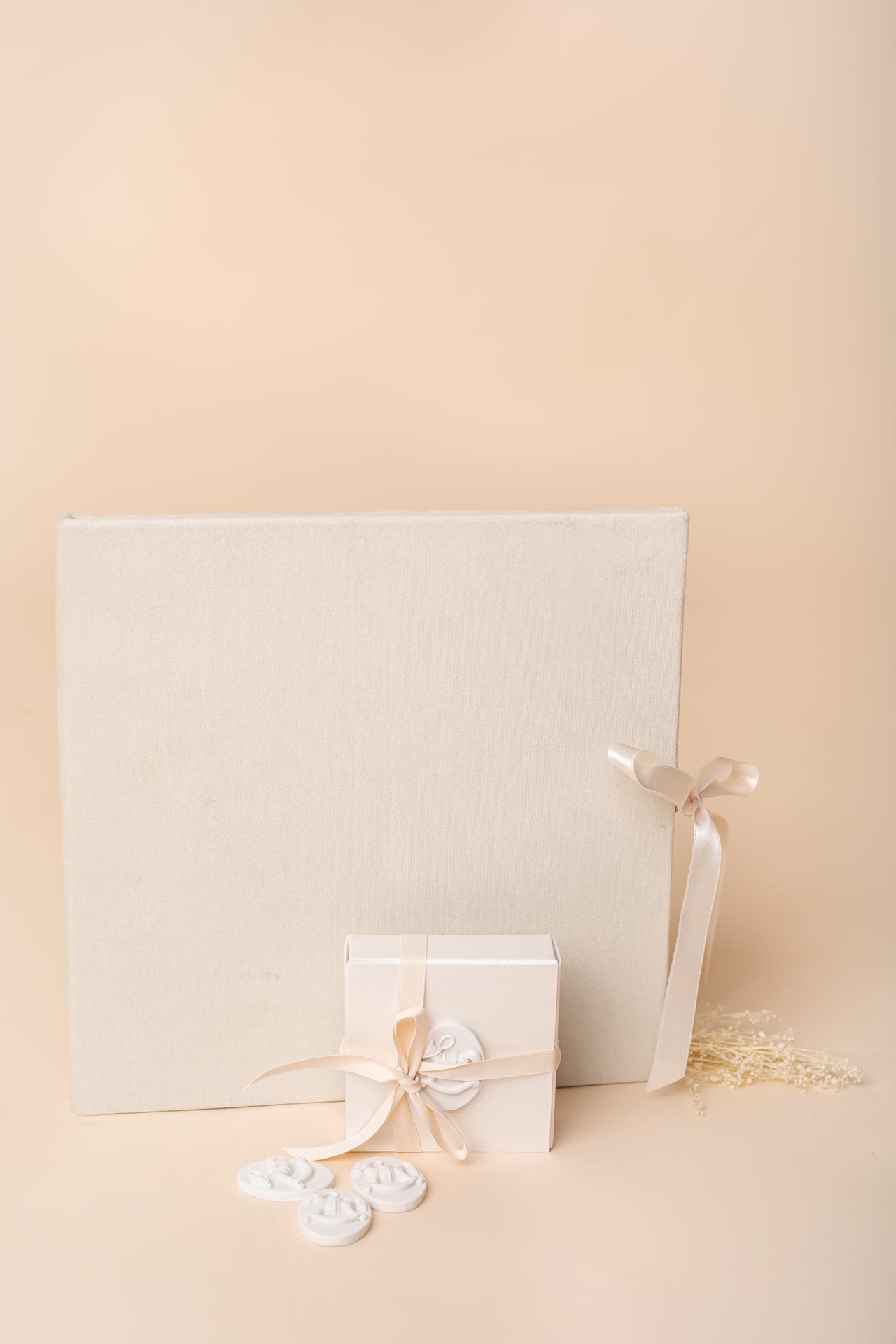 Álbum em veludo creme em pé com fita de cetim, ao lado de pequena caixa de prenda branca com selo de lacre e ramo de flores secas, produto signature Susana Schmitz Fotografia, Porto