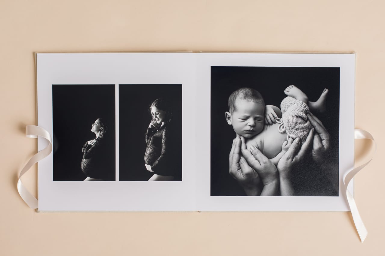 Spread interior do álbum signature aberto com duas impressões a preto e branco de sessão de gravidez em estúdio e uma impressão maior de recém-nascido cradled in hands, Susana Schmitz Fotografia