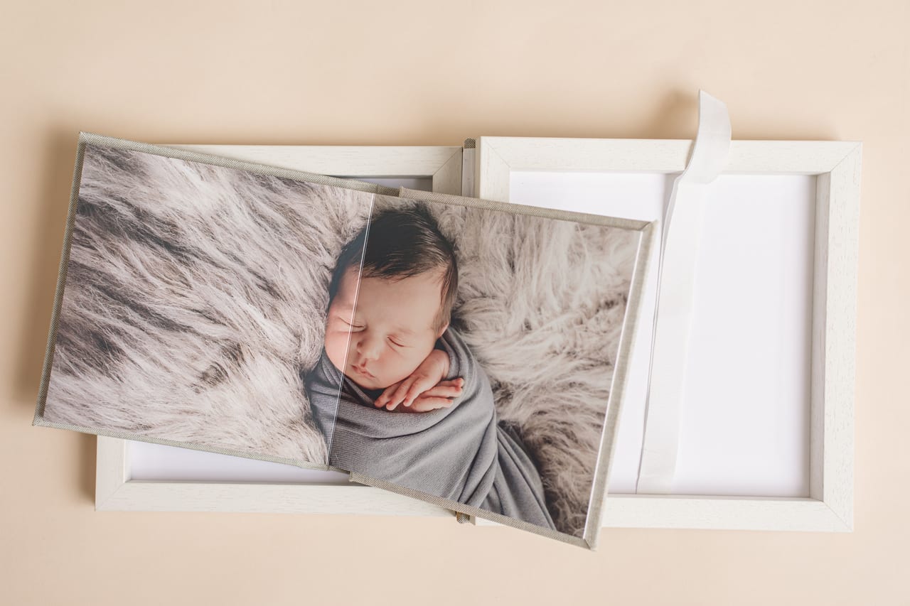 Duo Collection: caixa em madeira clara com fotografia de recém-nascido envolto em wrap cinza sobre tapete flokati, ao lado da segunda caixa com fita, produto Susana Schmitz Fotografia, Porto