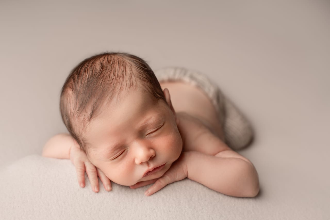 Recém-nascido a dormir em pose froggie sobre as próprias mãos, fundo bege suave, sessão em estúdio, Susana Schmitz Fotografia, Porto