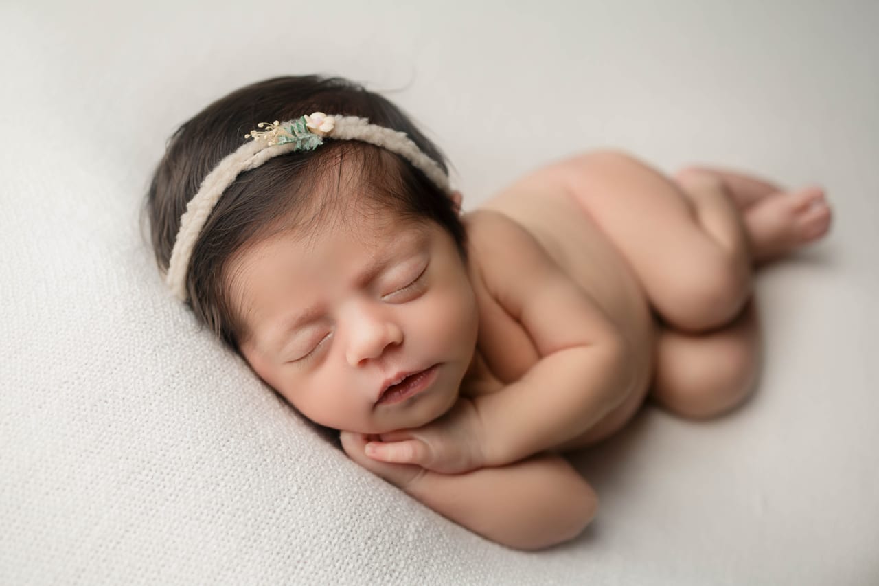Bebé recém-nascido com tiara floral creme a dormir em pose lateral sobre tecido cremoso liso, Susana Schmitz Fotografia