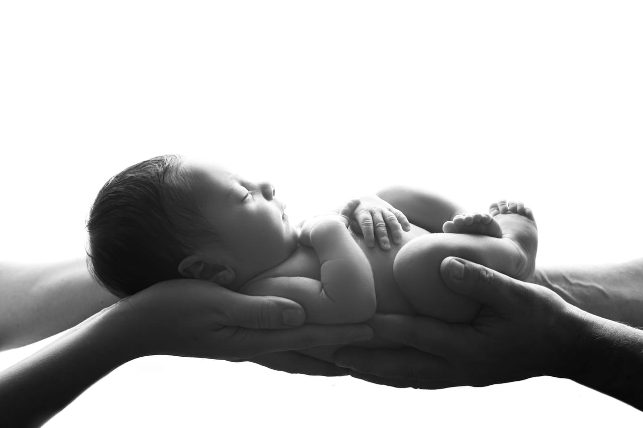 Recém-nascido a dormir nas mãos cruzadas dos pais em contraluz, retrato a preto e branco em estúdio, Susana Schmitz Fotografia